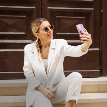 Frau in weißem Hosenanzug und Brille macht ein Selfie